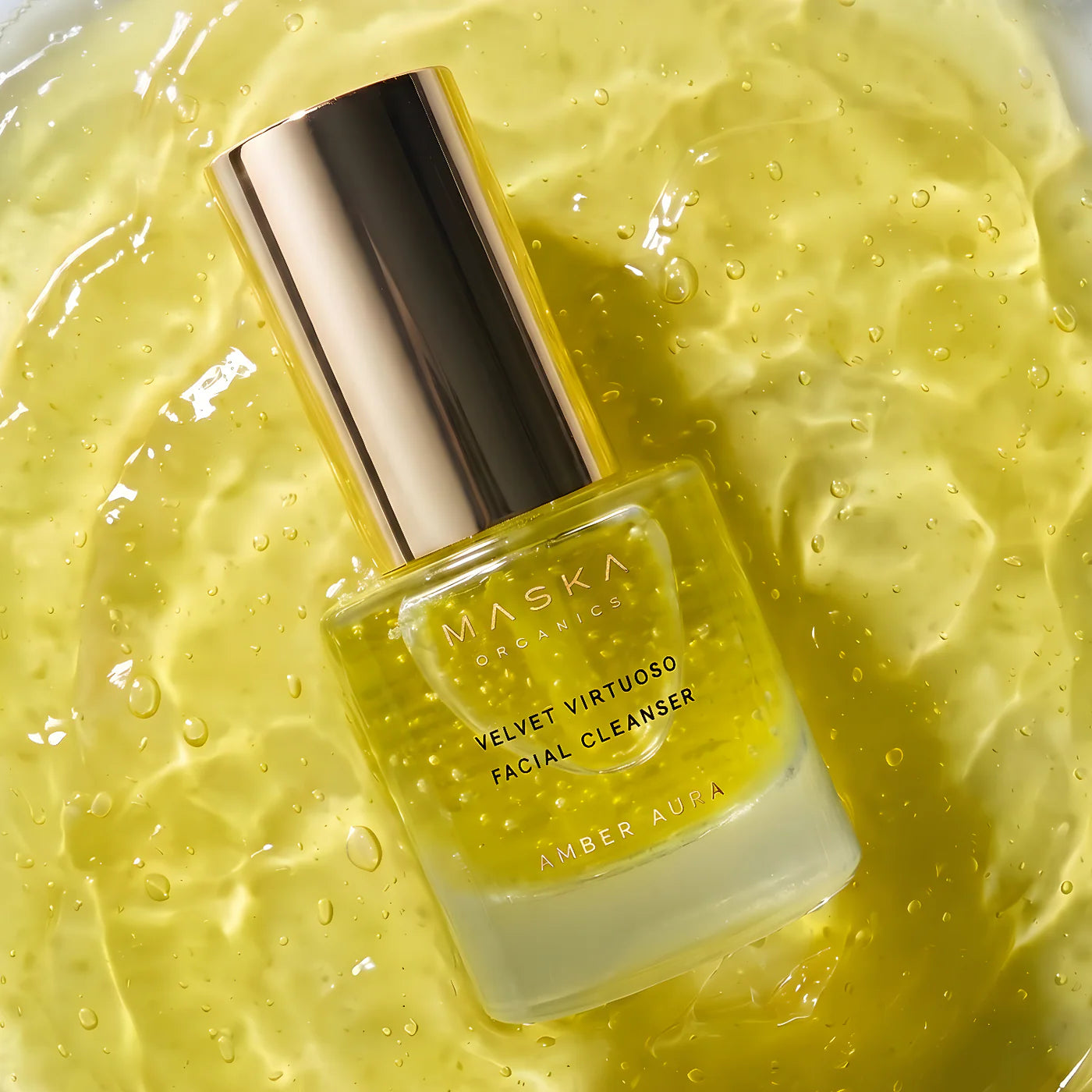Maska Organics Velvet Virtuoso Facial Cleanser bottle displayed on a rich golden gel texture with visible botanical particles and hydration droplets